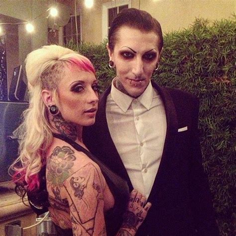 A Man In A Tuxedo Poses Next To A Woman With Tattoos On Her Arms