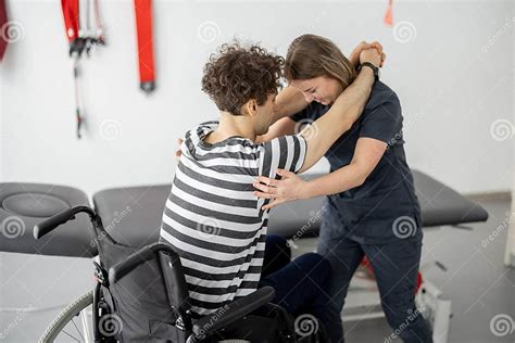 Nurse Of The Rehabilitation Center Helps Man To Get Up From A Wheelchair At Clinic Stock Image