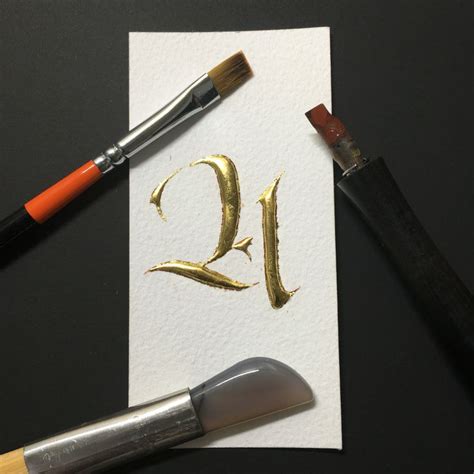 the letter q is painted gold on a piece of paper next to some paintbrushes