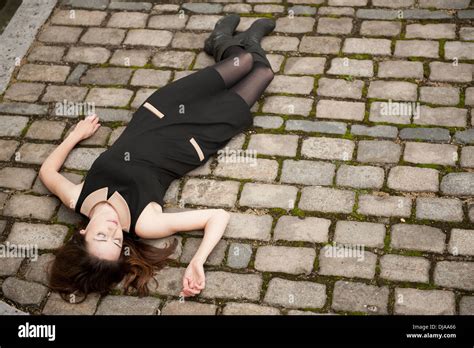 Elevated view of a woman wearing a black dress and lying down (dead?) on a cobbled road Stock ...