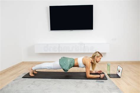 Fit Woman Doing Yoga Plank And Watching Online Tutorials On Laptop