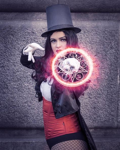 a woman wearing a top hat and holding a clock in front of her face while standing next to a wall