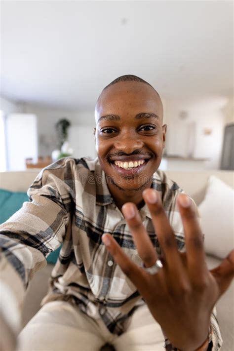 African American Gay Man With Short Hair Showing Wedding Ring While Sitting On Sofa In Living