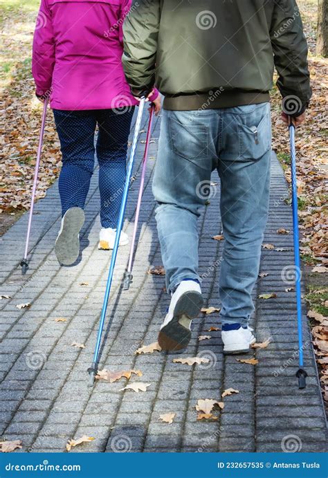 The Couple Are Marching In The Park With Nordic Walking Sticks Stock