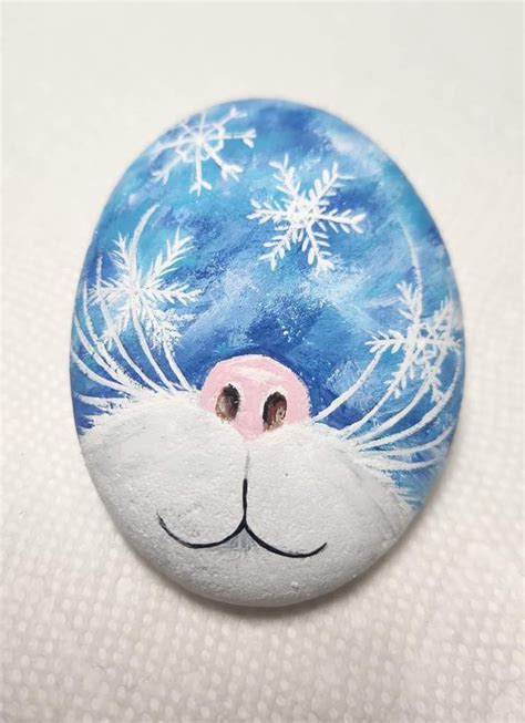 A Painted Rock With A Cat S Face And Snowflakes On It