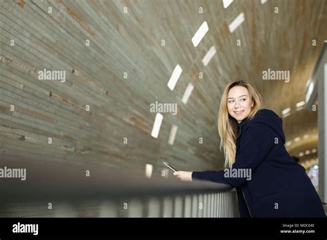 Blonde Female Student Standing With Modern Smartphone In Monophonic Illuminated Background Stock