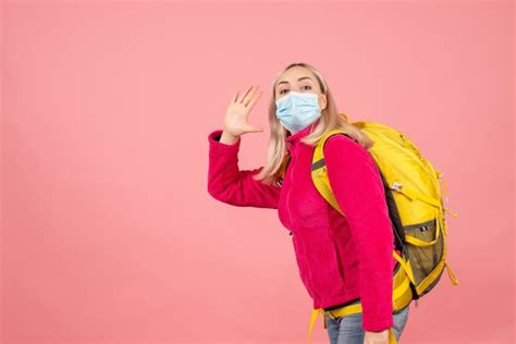 Vue de face femme blonde avec sac à dos jaune portant un masque en agitant la main Photo Gratuite