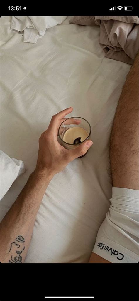 A Man Laying In Bed Holding A Cup Of Coffee