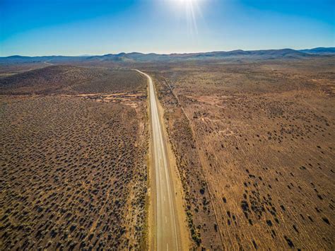 Rural Road Passing Through Dry Land With Scarce Vegetation On Bright