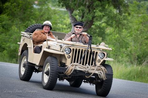 Two Men Riding In The Back Of An Old Jeep Down A Road With Trees Behind