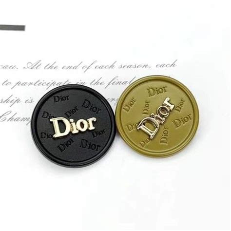 Two Black And Gold Buttons With The Word Dior Printed On Them Sitting