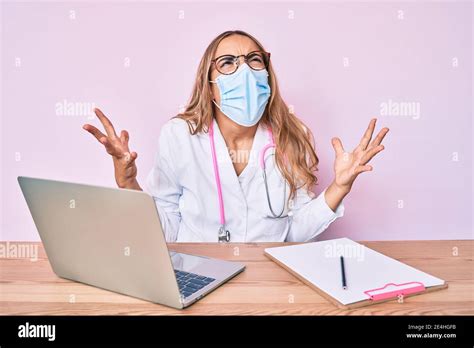 Jeune belle femme blonde portant l uniforme de médecin et le masque médical fou et fou criant et