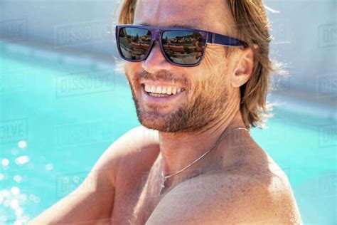 The Handsome Brutal Man In Sunglasses With A Long Hair And Naked Torso Sits Near The Pool Is