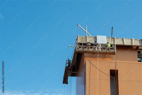 Using a construction gondola lift, workers place panels on a towering ...