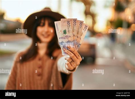 Brunette Woman Wearing Winter Hat Smiling Holding Colombian Pesos Banknotes Outdoors At The City