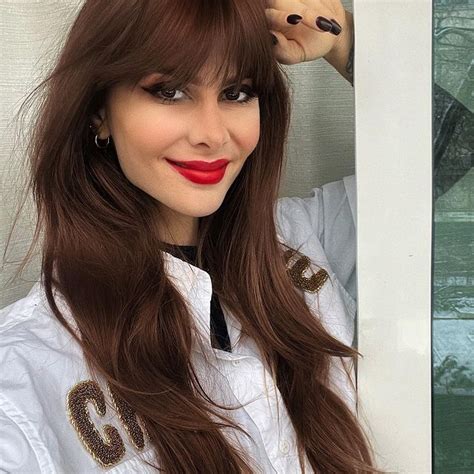 A Woman With Long Brown Hair Wearing A White Shirt And Red Lipstick Posing For The Camera