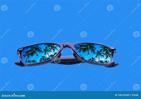 Sunglasses In A Black Frame With Palm Trees In The Reflection Of The Lenses On A Blue Background