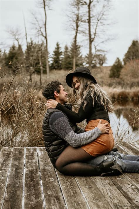 A Man And Woman Are Sitting On A Wooden Dock By The Water Hugging Each