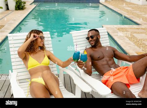 Couple Toasting Glasses Of Cocktail While Relaxing On A Sun Lounger