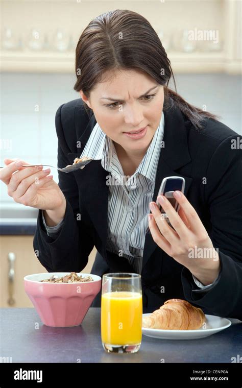 Brunette Female Sitting At A Kitchen Table Hair Tied Back Looking At Her Mobile Phone Confusion