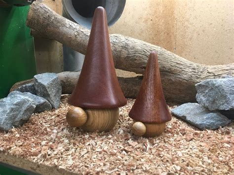 Two Wooden Gnomes Sitting On Top Of A Pile Of Wood