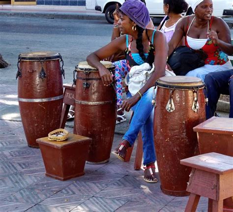 Three Women Sit On Stools And Play Musical Instruments In Front Of Some