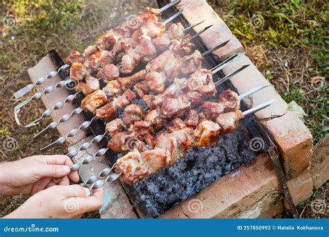 A Man Flips Pork Skewers Grilled Over Coals On A Brick Grill Delicious