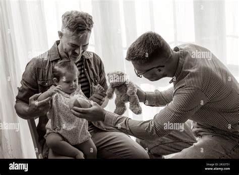 Male Gay Couple With Adopted Baby Girl At Home Two Handsome Fathers Playing With Their