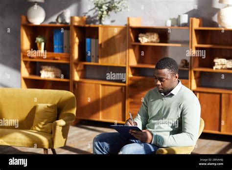 African Man Sitting On Chair And Making Notes In Document At The Office