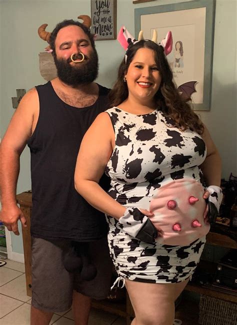 A Man Standing Next To A Woman In A Cow Print Dress With Horns On Her Head