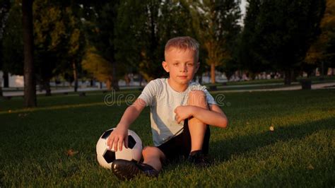 A Tired Little Boy is Sitting on the Green Grass in a Park with a Soccer Ball. Stock Footage ...