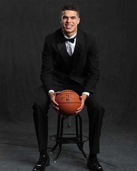 A Man In A Tuxedo Sitting On A Stool Holding A Basketball And Smiling