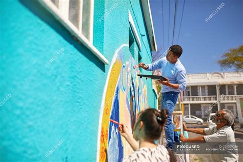 Community volunteers painting vibrant mural on sunny urban wall ...