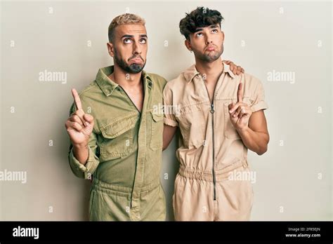 Homosexuel gay couple debout ensemble portant combinaison décontractée pointant vers le haut l