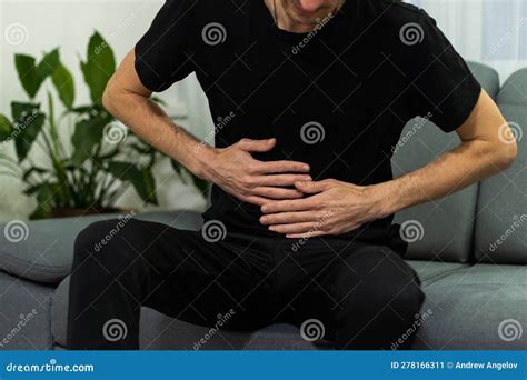 Man Suffering With Severe Stomach Pain Sitting At Home Hand Of Mature