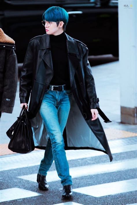 a man with blue hair walking across a cross walk holding a black bag ...