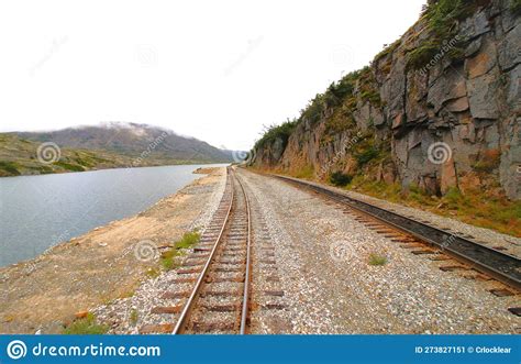 Train Tracks Running Through A Mountain Range With A Stream Flowing