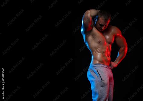 Male Bodybuilder Athlete With Naked Torso Posing Against A Black Background In Red And Blue