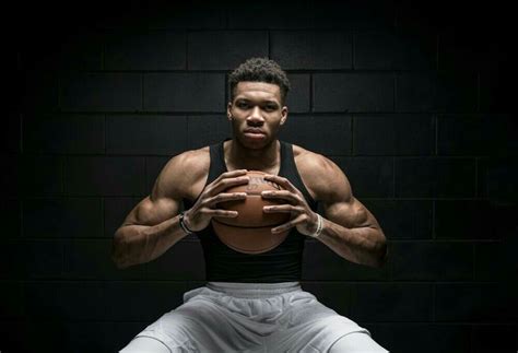 A Man Holding A Basketball In Front Of A Brick Wall With His Hands On