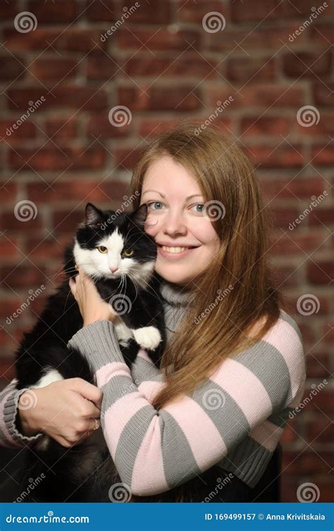 Chica Sonriente Sobre Un Fondo De Pared De Ladrillo Con Un Gato Blanco Y Negro En Las Manos