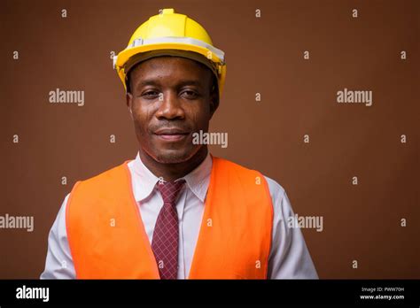 Young African Man Construction Worker Against Brown Background Stock