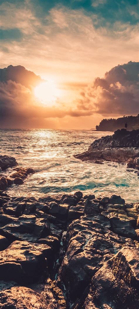 The Sun Is Setting Over The Ocean With Rocks In Front Of It And Some Water