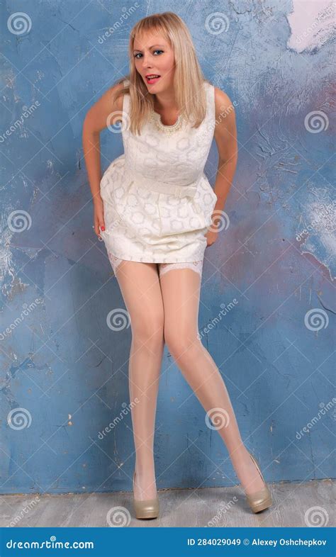 Beautiful Blonde Girl With Long Legs In White Stockings And High Heels Posing At The Wall Stock
