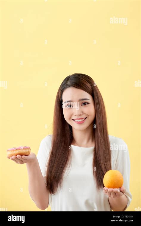 Portrait Of A Smiling Young Asian Woman Choosing Between Donut And