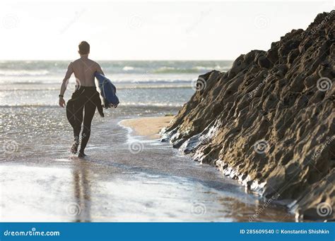 A Man With A Naked Torso Walking On The Beach Holding A Surfboard View From The Back Stock