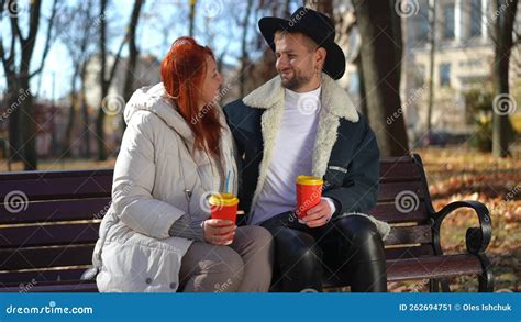 Hugging Mature Mother And Adult Son Sitting On Bench In Sunshine Looking At Each Other Smiling