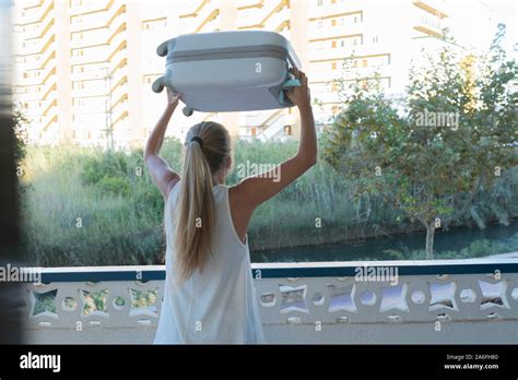 Vue arrière d une femme blonde levage d une valise gris sur sa tête sur une terrasse de l hôtel