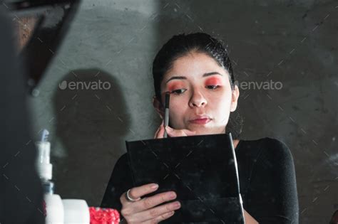 Latina Woman Looking At Herself In Front Of The Mirror Holding The Mirror Of Her Eye Shadow