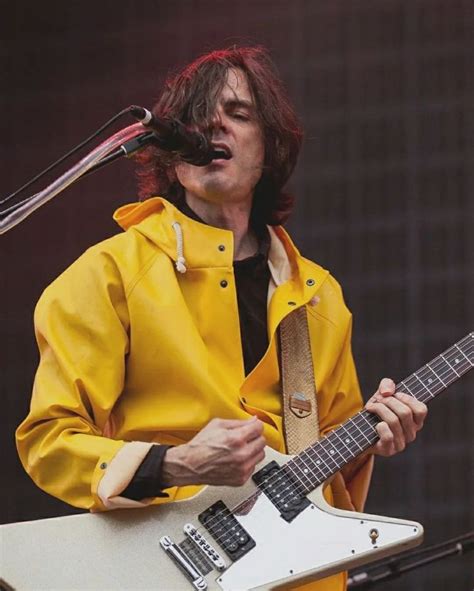 A Man In Yellow Jacket Playing An Electric Guitar At A Music Festival