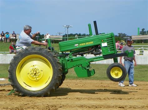 A Man Driving A Green Tractor On Top Of A Dirt Field